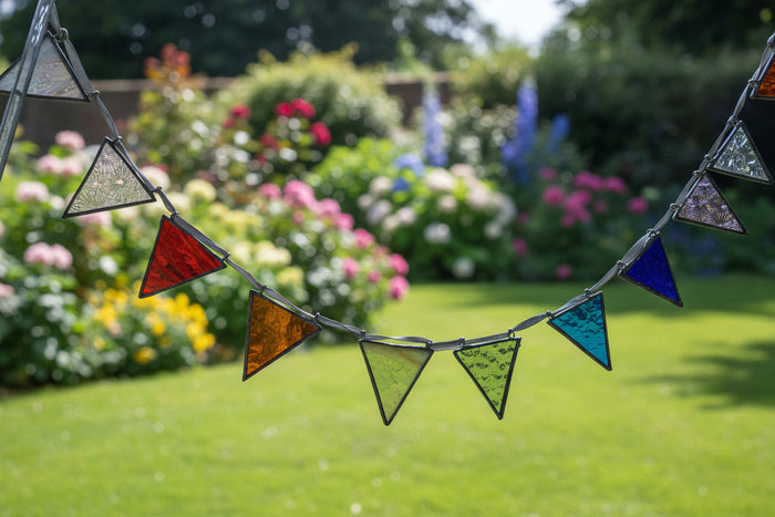 A stained glass arch suncatcher with multiple colorful triangular panes in blue, green, orange, red, and purple, suspended on a metal frame in front of a window.