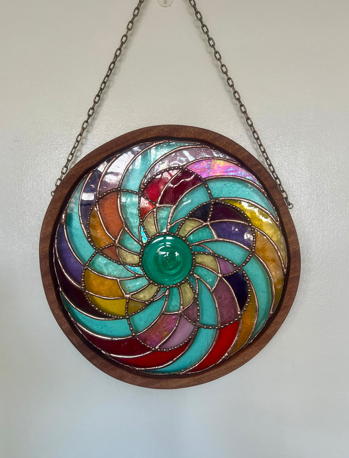 Pinwheel designed multi coloured stained glass suncatcher surrounded by a circular wooden frame 