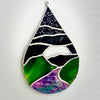 A teardrop-shaped stained glass hanging ornament depicting a landscape with green hills, a purple valley, and a dark blue sky, set against a plain white wall.