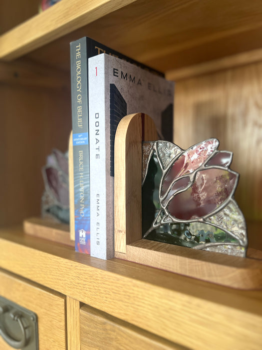 A close-up of a wooden bookshelf holding two books, including Emma Ellis's 'The Biology of Beauty' and 'Donate', with a stained-glass tulip holder on the shelf.