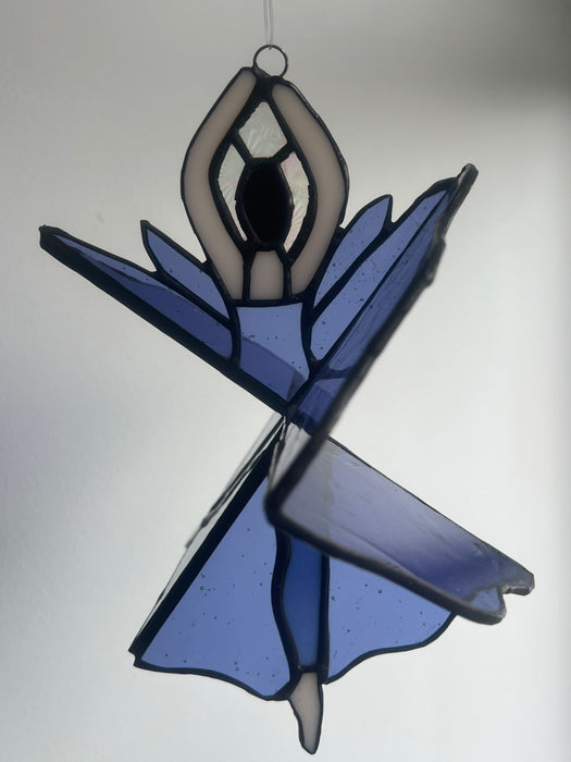 A stained glass suncatcher depicting a dancing female figure in shades of blue, lavender, and cream, outlined with dark lead lines.