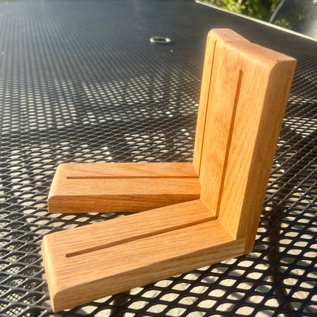 A pair of light oak wood corner brackets with a smooth finish and visible wood grain, resting on a black metal mesh patio table.