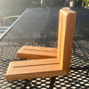 A handmade L-shaped wooden corner bracket made from natural oak wood, resting on a black metal mesh patio table outdoors.
