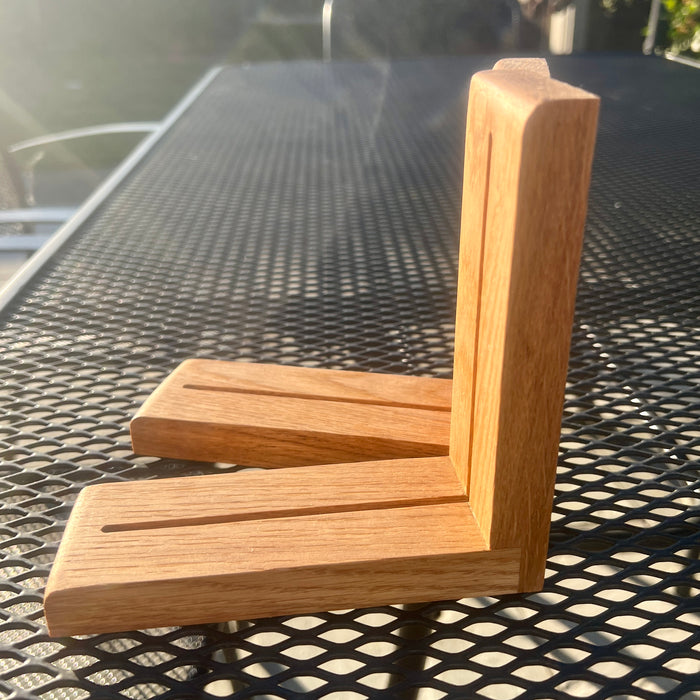 A handmade L-shaped wooden corner bracket made from natural oak wood, resting on a black metal mesh patio table outdoors.