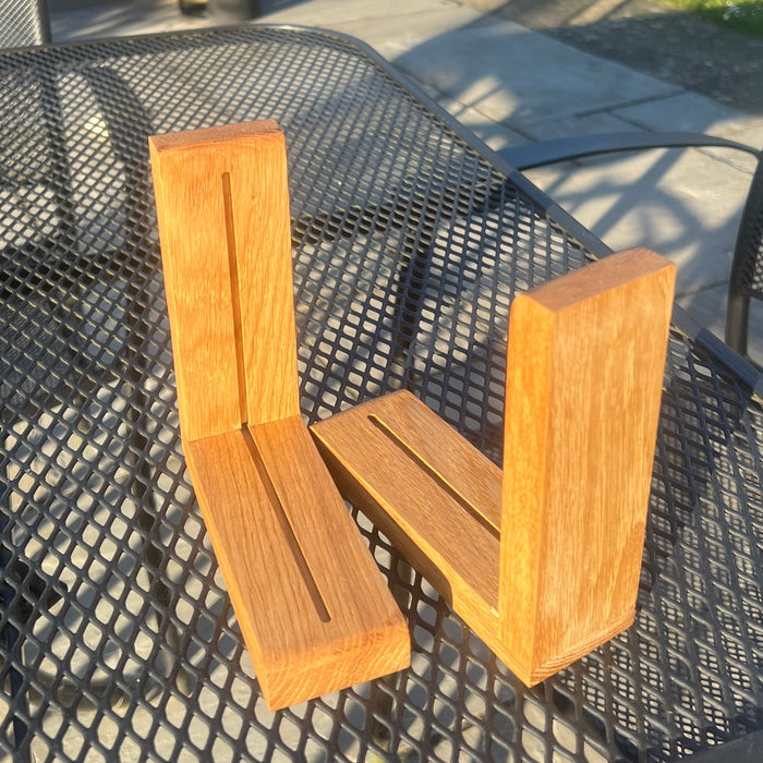 Two light brown wooden bookends with a visible wood grain, displayed on a black metal mesh patio table outdoors.