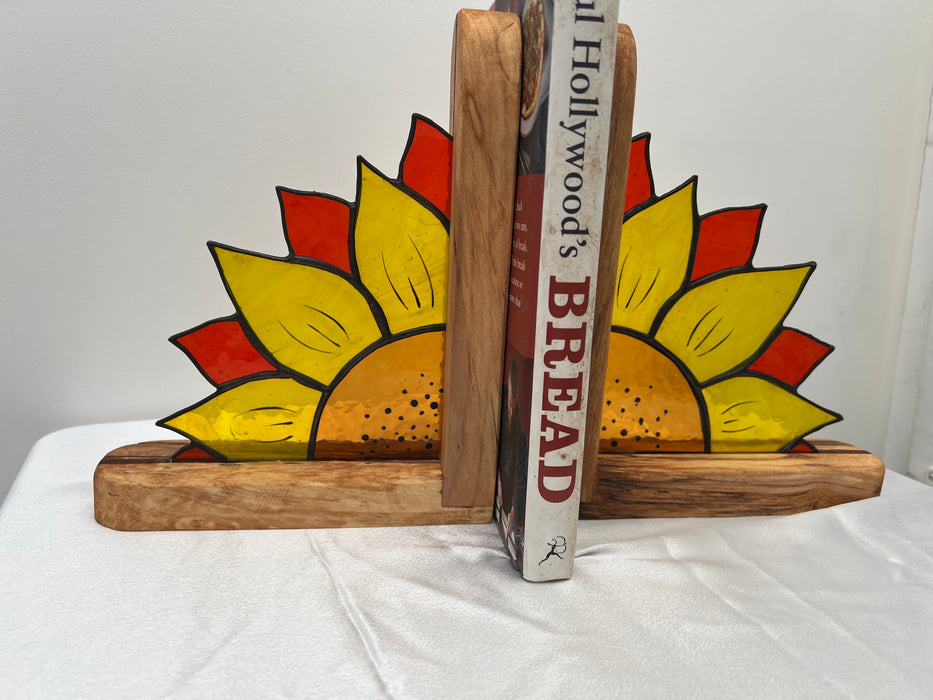 Hand-painted wooden sunflower bookends holding up two books on a white fabric-covered surface against a plain white background.