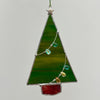 A hanging stained glass Christmas tree ornament with a green body, silver metal frame, a silver star topper, and small multicolored glass bead lights, shown against a plain light gray background.