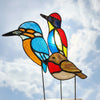 three stained glass bird sculptures on metal stands, featuring colorful bird designs with blue, red, yellow, orange, white, and brown panels separated by dark lead lines, displayed indoors