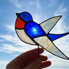 A hand holding a stained glass swollow suncatcher with blue, white, and orange sections outlined in black铅.