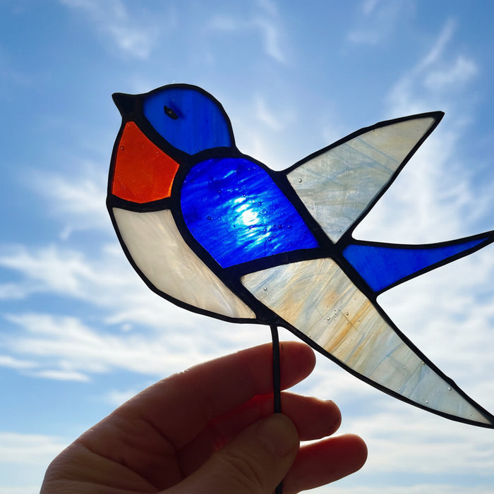 A hand holding a stained glass swollow suncatcher with blue, white, and orange sections outlined in black铅.