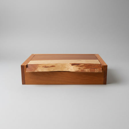A rectangular wooden storage box with a hinged lid, featuring a rich reddish-brown wood body and a lighter natural wood inlay on the lid, set against a neutral gray background.