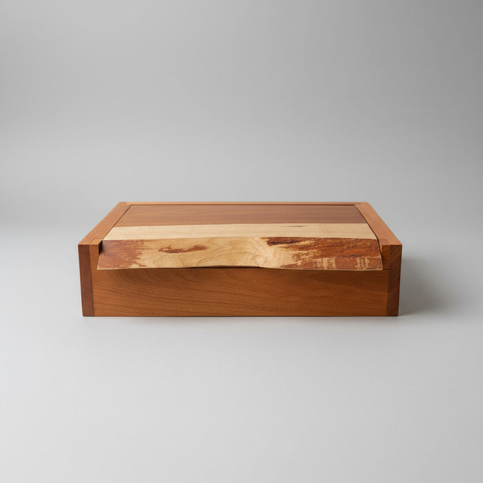 A rectangular wooden storage box with a hinged lid, featuring a rich reddish-brown wood body and a lighter natural wood inlay on the lid, set against a neutral gray background.