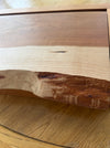 A close-up of a live-edge wood slab showing a natural transition from pale beige wood on the left to medium brown and dark reddish-brown on the right, set against a background of a similar wood grain surface.
