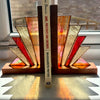 Two Art Deco style bookends made of stained glass and wood, holding up a book on a windowsill.