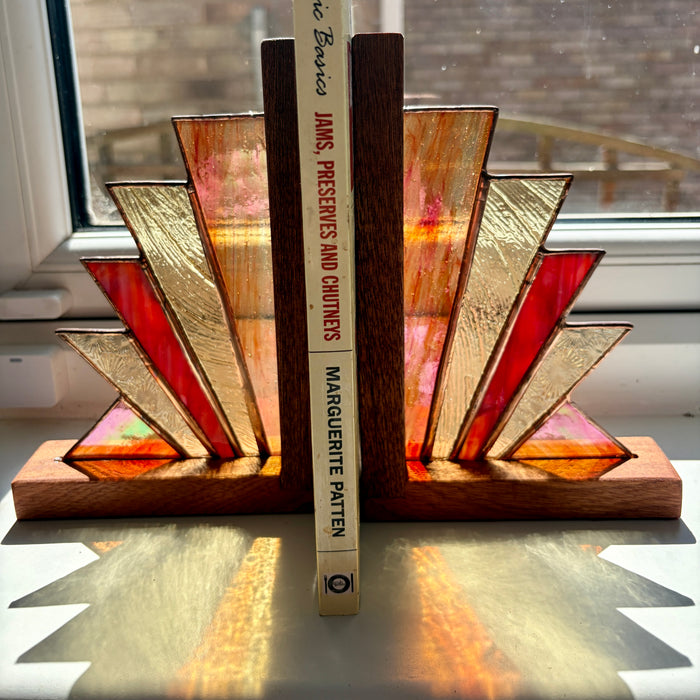 Two Art Deco style bookends made of stained glass and wood, holding up a book on a windowsill.
