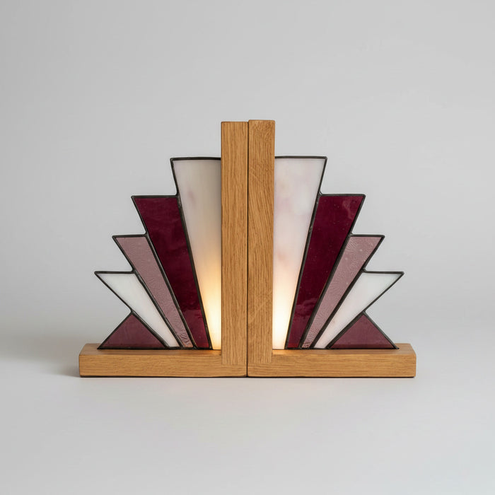 A stained glass bookend with geometric fan-shaped panels in burgundy, white, and lavender, held together by two vertical oak wood posts on a matching oak base, set on a light marble countertop.