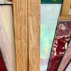 Close-up of stained glass panels with a prominent light oak wood frame in the center, flanked by cream, iridescent blue-green, and deep burgundy glass sections.