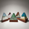 Three handmade stained glass pyramid mountain sculptures on wooden bases, displayed on a white kitchen countertop.