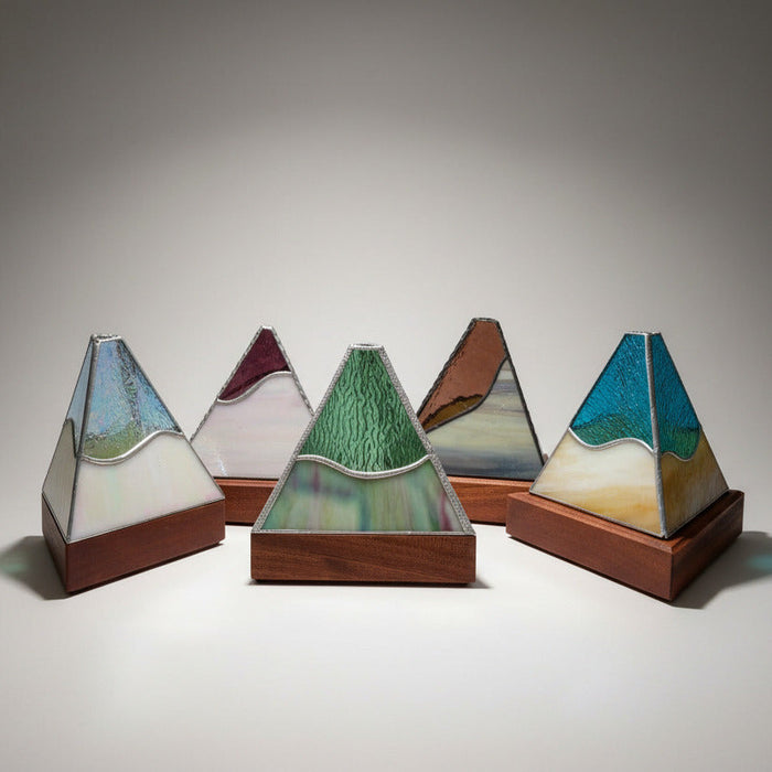 Three handmade stained glass pyramid mountain sculptures on wooden bases, displayed on a white kitchen countertop.