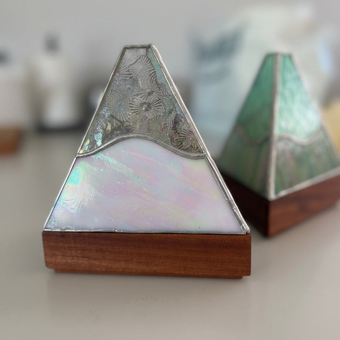 Two triangular decorative boxes with iridescent abalone shell panels, silver-toned metal borders, and wooden bases, shown on a light tabletop with a softly blurred background.