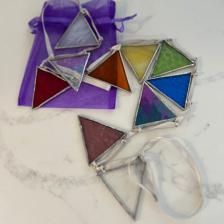 A set of triangular stained glass window bunting with silver metal frames, shown on a white marble surface next to a purple organza bag.