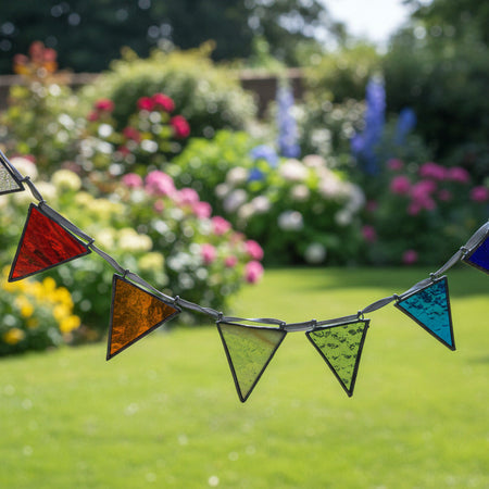 A stained glass arch suncatcher with multiple colorful triangular panes in blue, green, orange, red, and purple, suspended on a metal frame in front of a window.