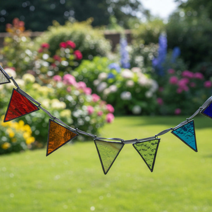 A stained glass arch suncatcher with multiple colorful triangular panes in blue, green, orange, red, and purple, suspended on a metal frame in front of a window.