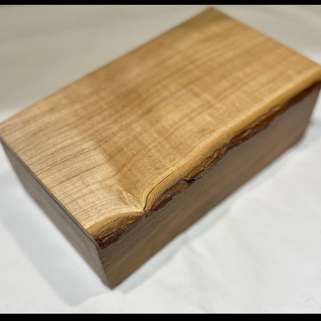 A rectangular wooden box with a live edge, showcasing a prominent natural grain on the top lid, photographed on a white fabric background.