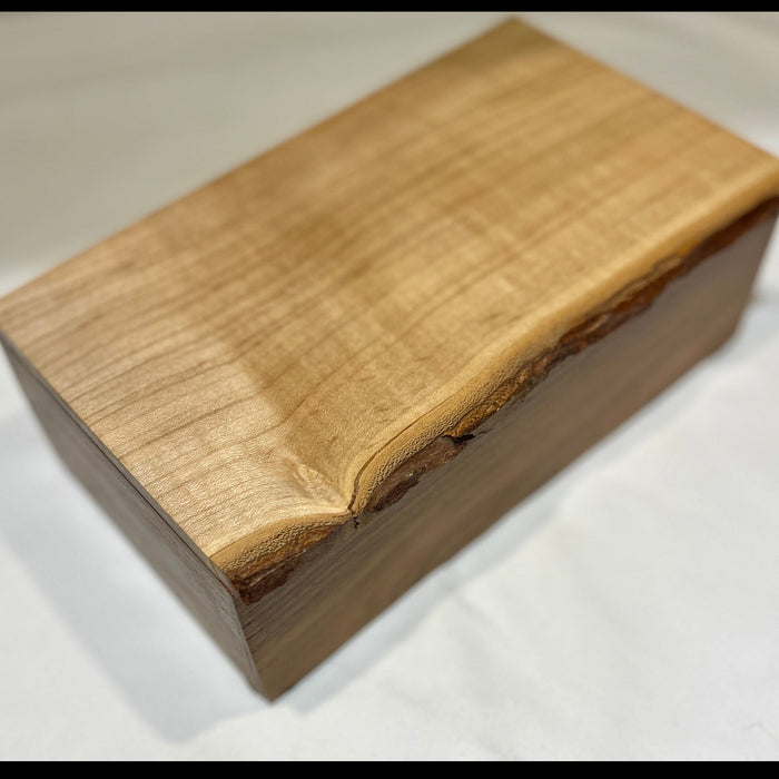 A rectangular wooden box with a live edge, showcasing a prominent natural grain on the top lid, photographed on a white fabric background.