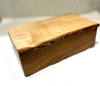 A rectangular wooden box with a live edge, featuring a light tan top and a darker brown side, photographed on a white surface with a soft-focus background.