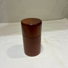 A small cylindrical wooden container with a matching lid, made of dark reddish-brown wood, standing on a white fabric surface.
