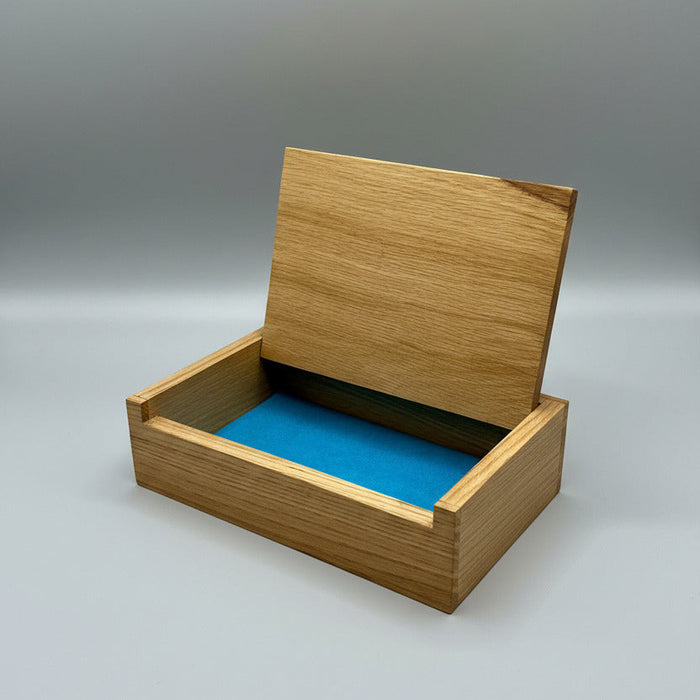 A rectangular wooden box with a hinged lid, shown open with a bright blue velvet or felt lining. The box is photographed on a white cloth surface with a blurred indoor background.
