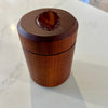 A small cylindrical wooden box with a lid, photographed on a white marble-like countertop. The top of the lid has a recessed oval area showing a brown polished agate piece.
