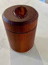 A small cylindrical wooden box with a lid, photographed on a white marble-like countertop. The top of the lid has a recessed oval area showing a brown polished agate piece.