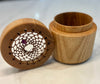 A wooden keepsake box with its lid off, showing a natural wood grain exterior and a decorative inner tray with a web-like pattern and a small purple gemstone.