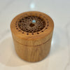 A small round wooden box with a lid featuring a decorative laser-cut lace pattern and a tiny light blue stone accent in the center, set on a light marble surface.